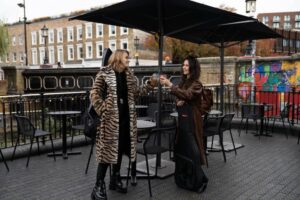  Los autónomos pueden reclamar el ITP por terrazas en suelo público, como esta donde dos mujeres brindan en un entorno urbano con mesas y sombrillas.